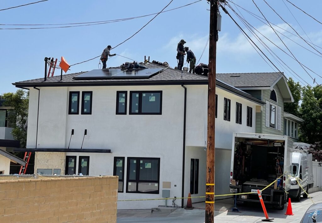 A picture of a house with a new ADU on the side and man working on the roof.